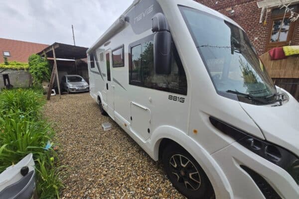 Camping-car blanc stationné dans une cour gravillonnée