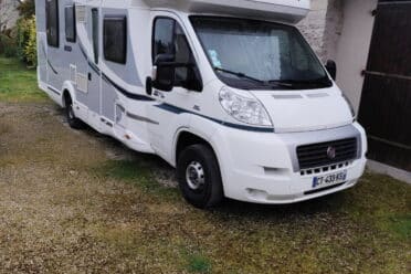 Camping-car blanc stationné près d'une maison