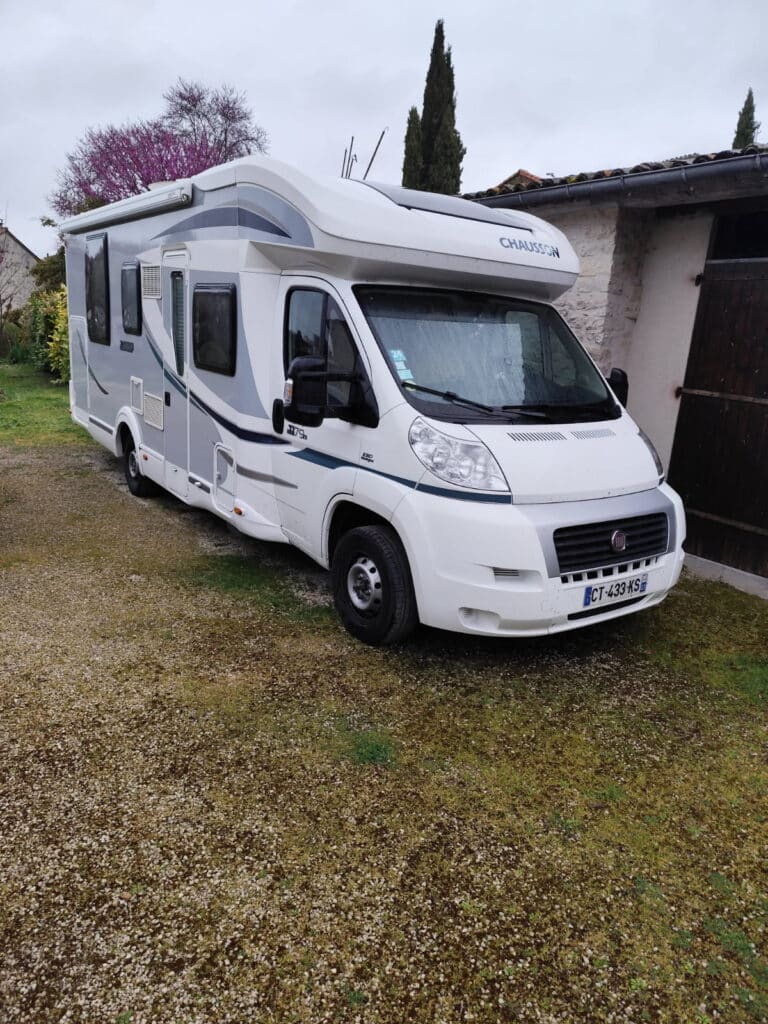 Camping-car blanc stationné près d'une maison