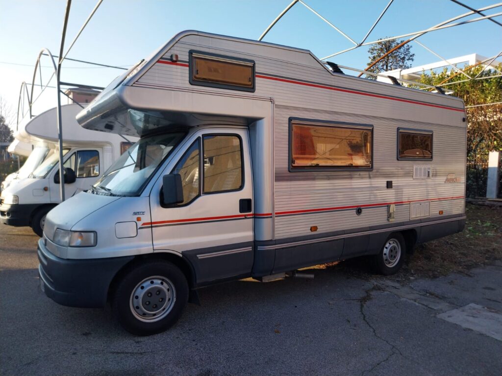 Camping-car blanc stationné en extérieur sous structure métallique
