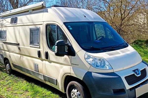 Camping-car Peugeot beige stationné dans un champ