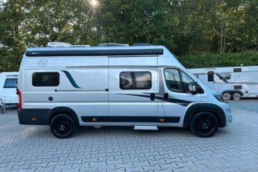 Van aménagé argenté stationné sur parking arboré
