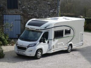 Camping-car blanc garé devant maison en pierre