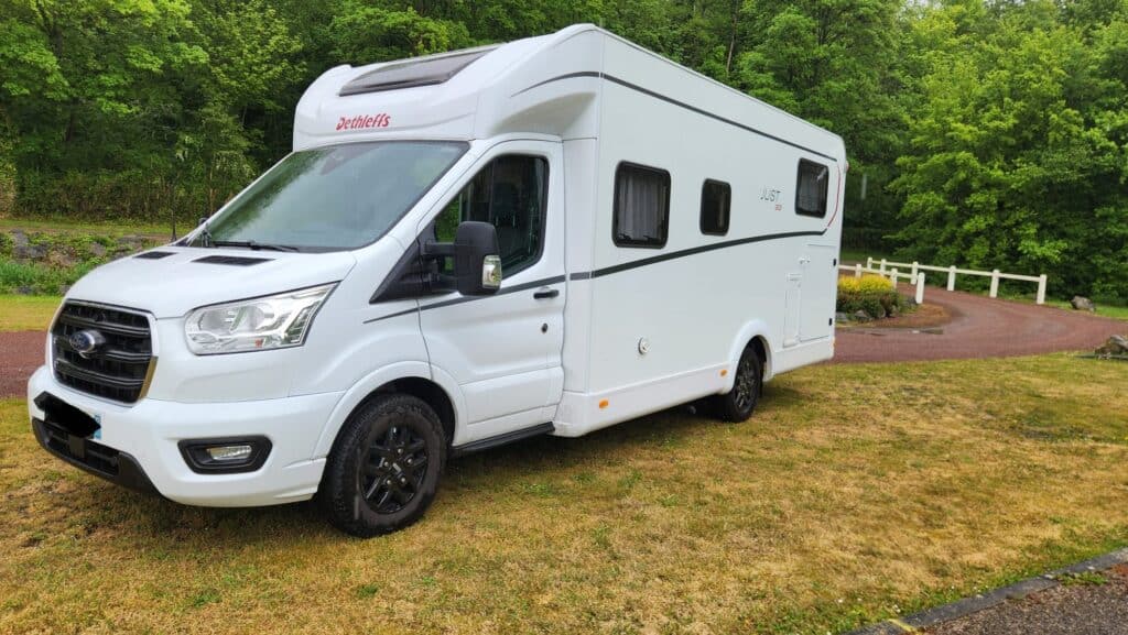 Camping-car blanc stationné près d’une forêt verdoyante