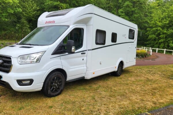 Camping-car blanc stationné près d’une forêt verdoyante