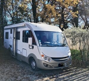 Camping-car blanc stationné sous des arbres d’automne