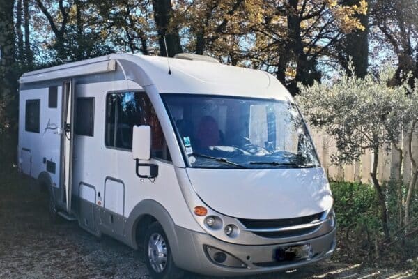 Camping-car blanc stationné sous des arbres d’automne