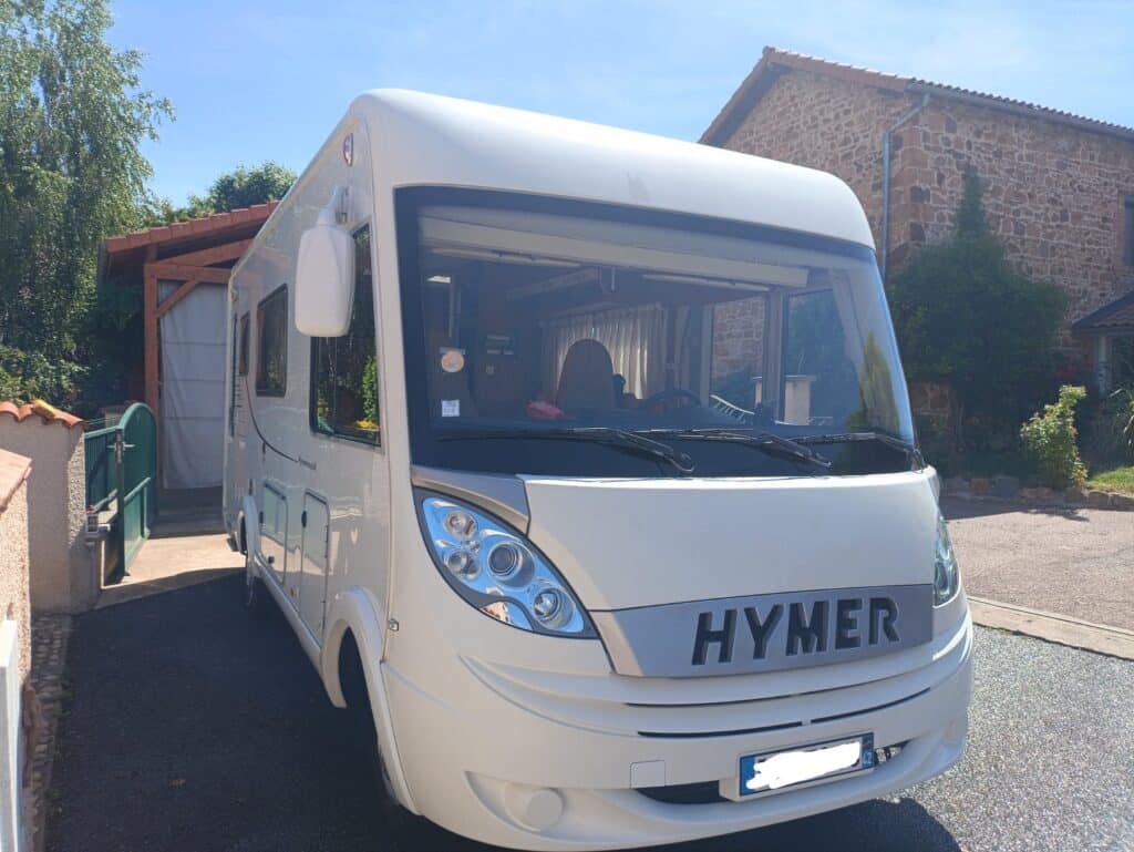 Camping-car blanc Hymer garé devant maison en pierre