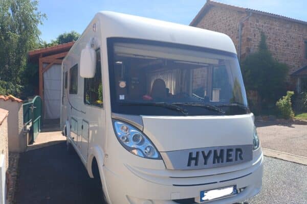 Camping-car blanc Hymer garé devant maison en pierre