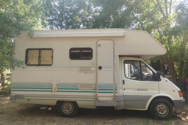 Camping-car blanc stationné sous des arbres