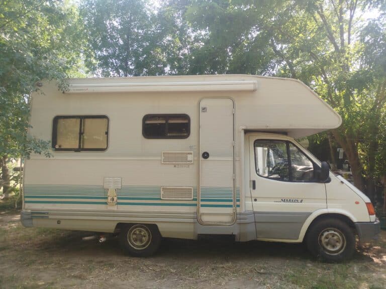 Camping-car blanc stationné sous des arbres