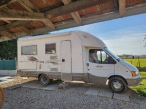 Camping-car blanc stationné sous un abri en bois