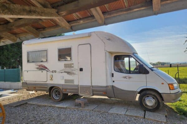 Camping-car blanc stationné sous un abri en bois