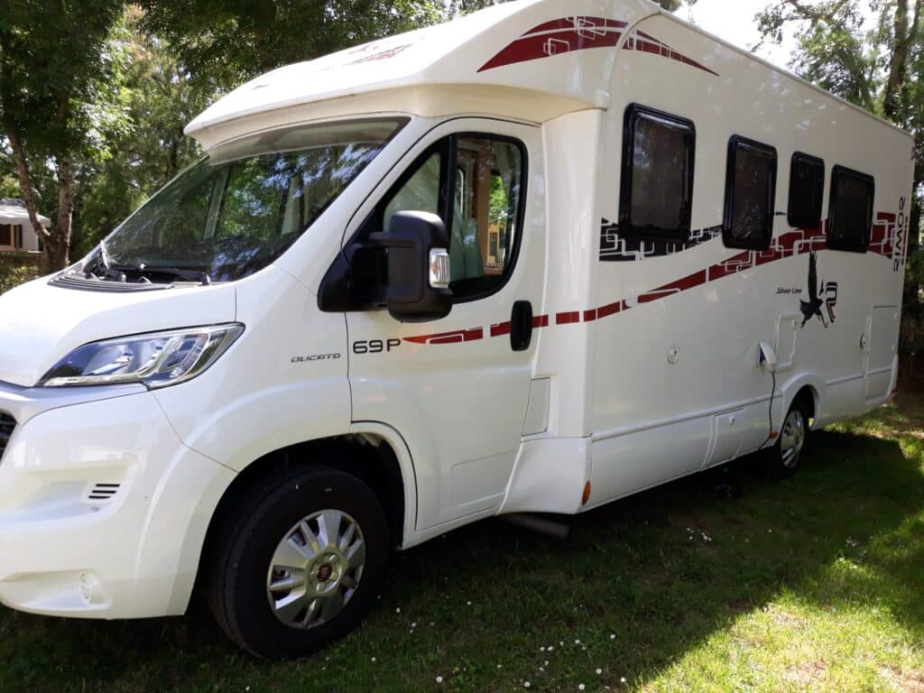 Camping-car blanc stationné sous des arbres