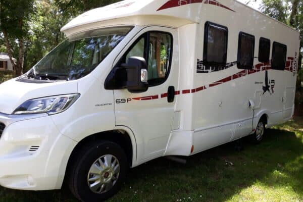 Camping-car blanc stationné sous des arbres