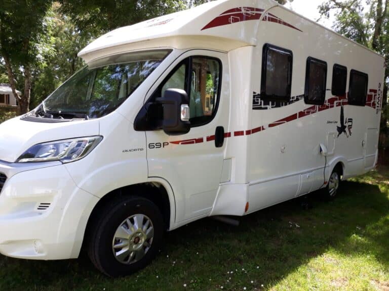 Camping-car blanc stationné sous des arbres