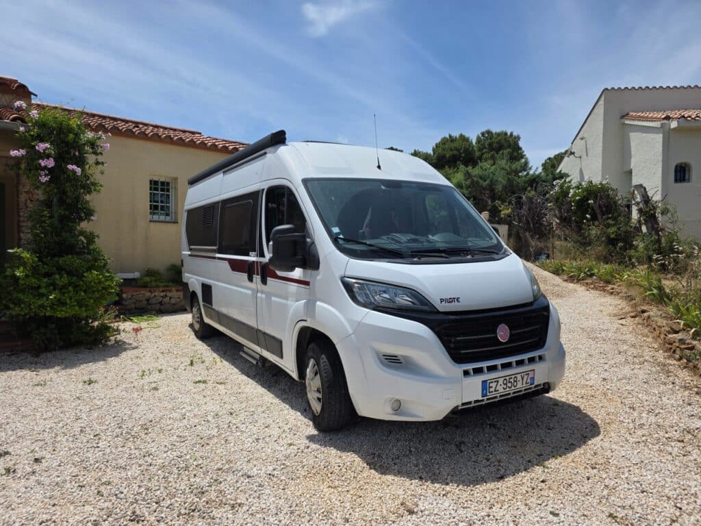 Fourgon aménagé blanc garé devant maison méditerranéenne