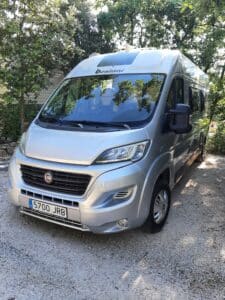 Camping-car Benimar argenté stationné sous des arbres