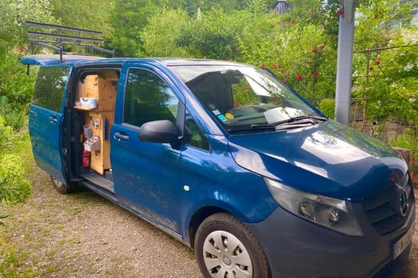 Van aménagé bleu garé dans un jardin