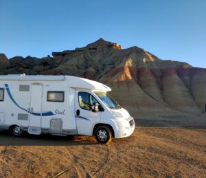Camping-car blanc devant collines désertiques au coucher du soleil