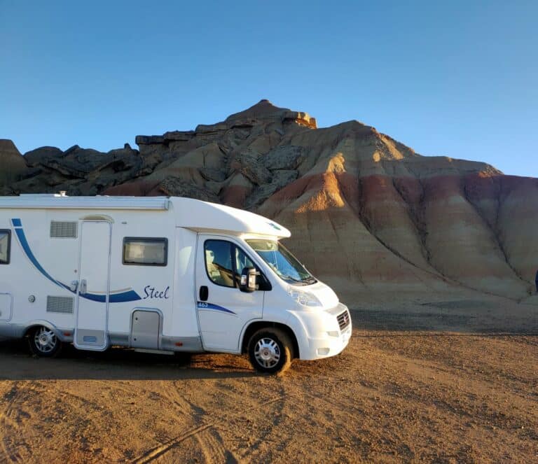 Camping-car blanc devant collines désertiques au coucher du soleil