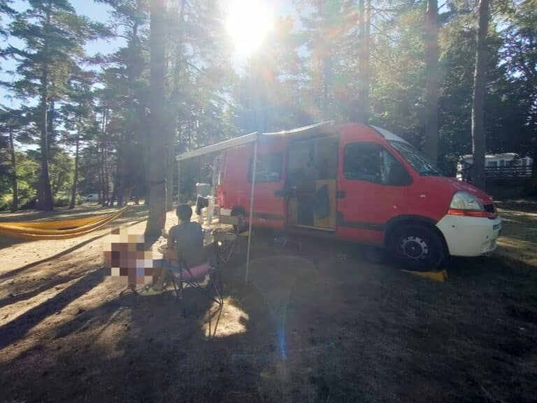 Van aménagé rouge en camping forestier ensoleillé