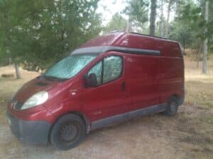 Fourgon rouge garé en forêt avec pare-soleil