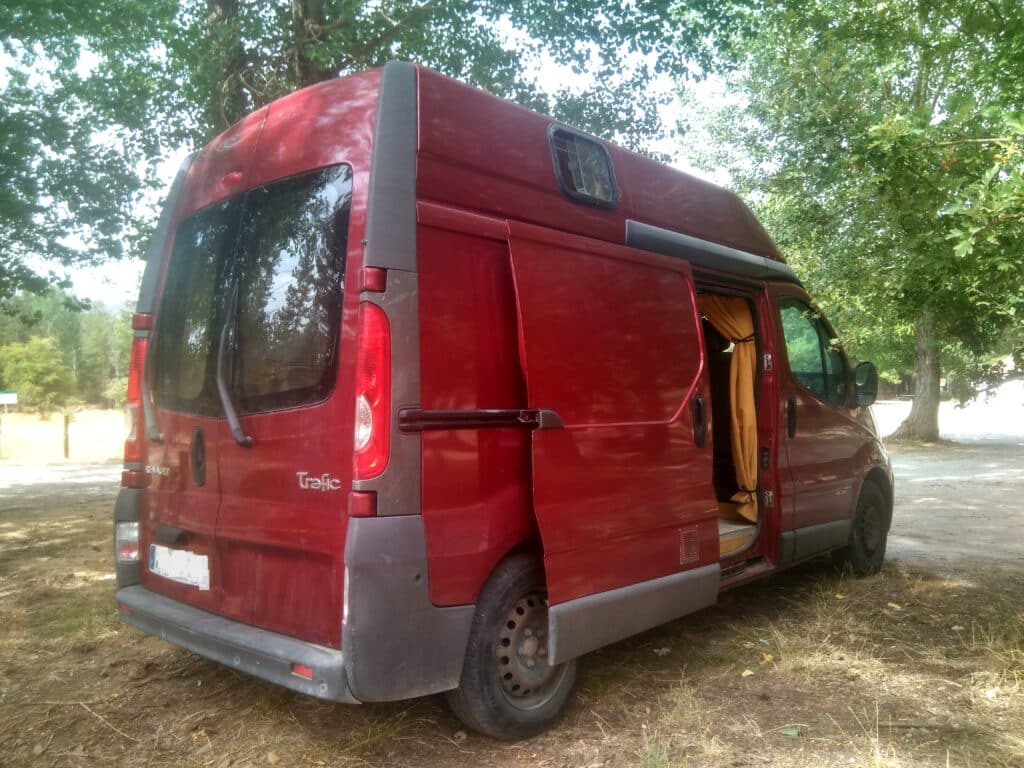 Fourgon rouge aménagé garé sous des arbres