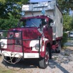 Camion rouge ancien transformé en camping-car, stationné.