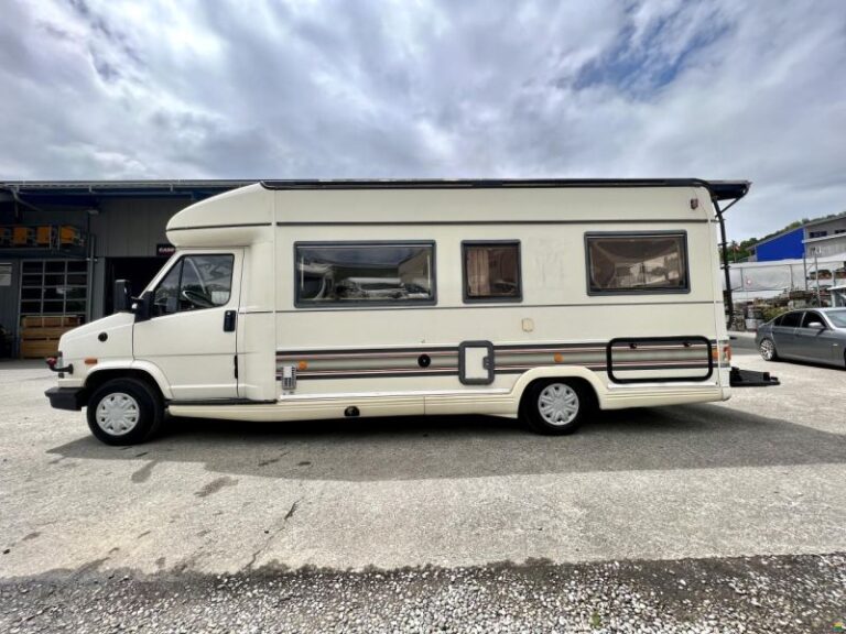 Camping-car blanc stationné, ciel nuageux.