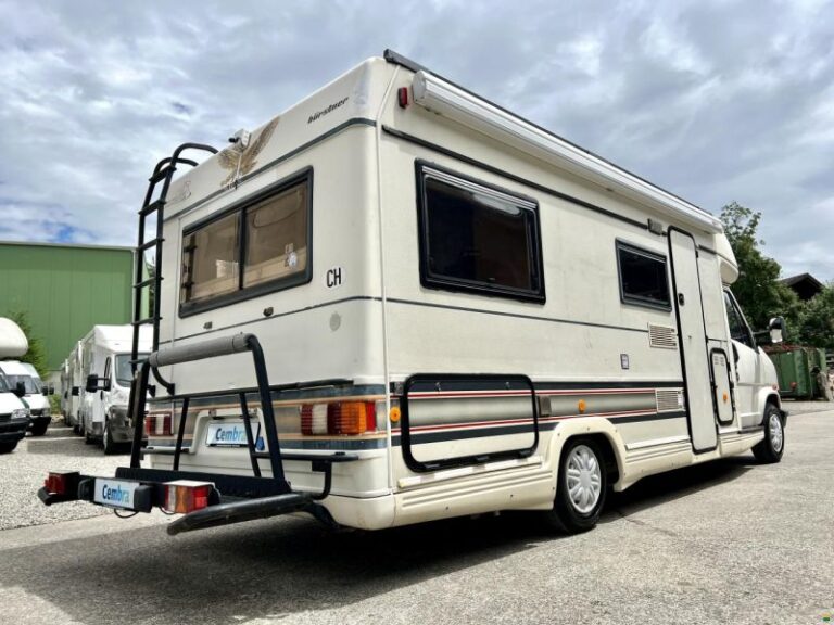 Camping-car blanc stationné, extérieur jour.