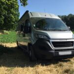 Camping-car gris garé près des champs verdoyants.