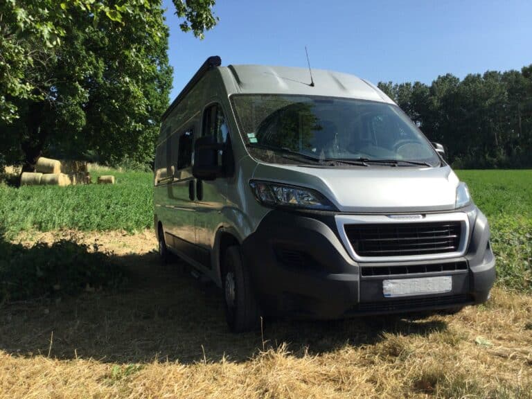 Camping-car gris garé près des champs verdoyants.