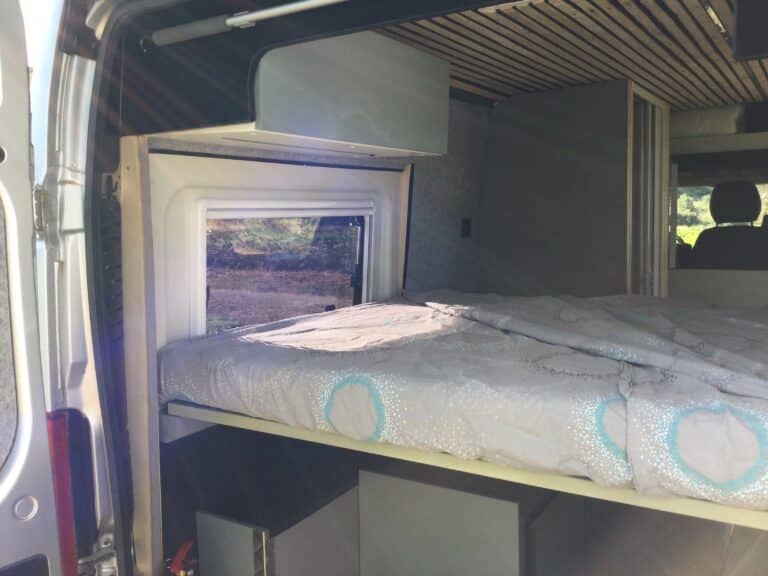 Intérieur d'un van aménagé avec lit et rangement.