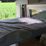 Intérieur de caravane avec lit et fenêtre ouverte.