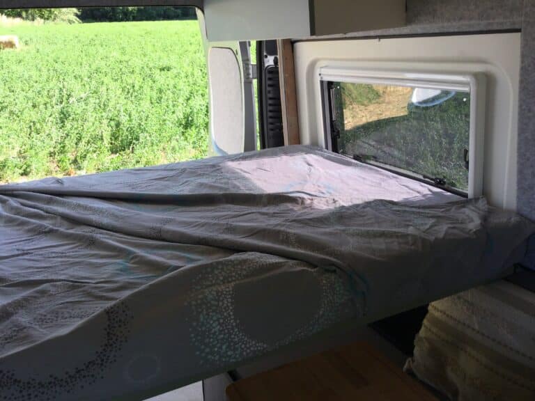 Intérieur de caravane avec lit et fenêtre ouverte.