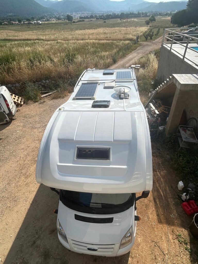 Camping-car blanc avec panneaux solaires sur le toit.