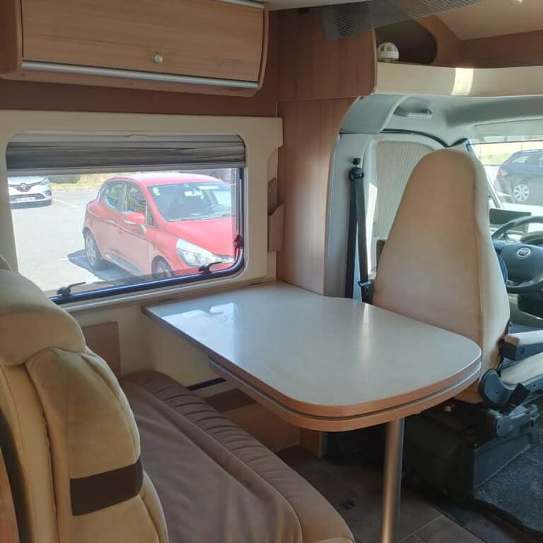 Intérieur d'un camping-car avec vue sur voiture rouge.