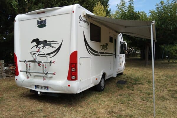 Wohnmobil weiß mit ausgebreitetem Vorzelt in einem Garten.