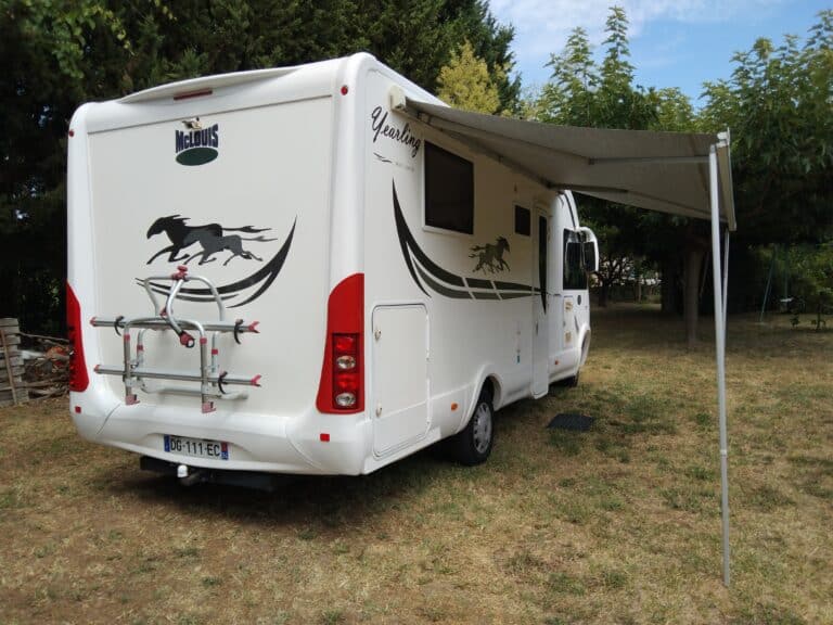 Camping-car blanc avec auvent déployé dans un jardin.