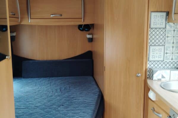 Intérieur de caravane avec lit et cuisine aménagée.