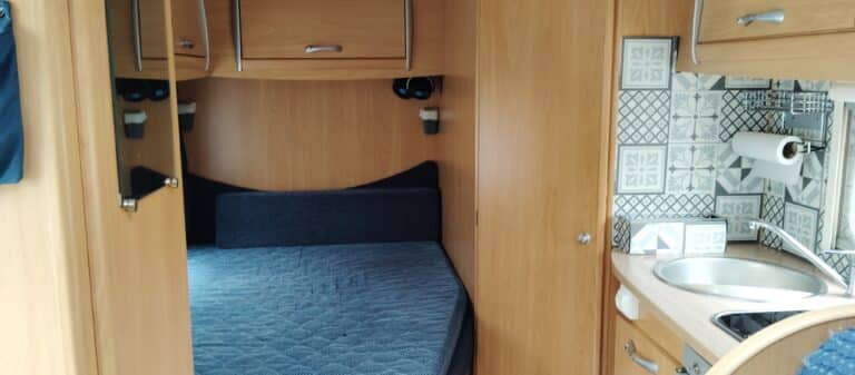Intérieur de caravane avec lit et cuisine aménagée.