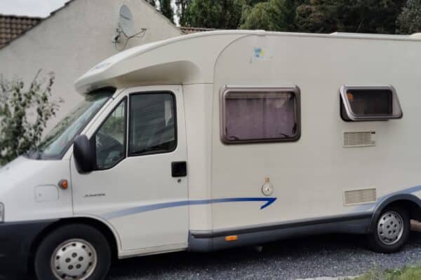 Camping-car stationné devant une maison blanche.