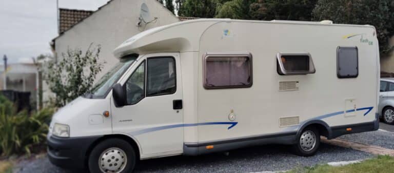 Camping-car stationné devant une maison blanche.