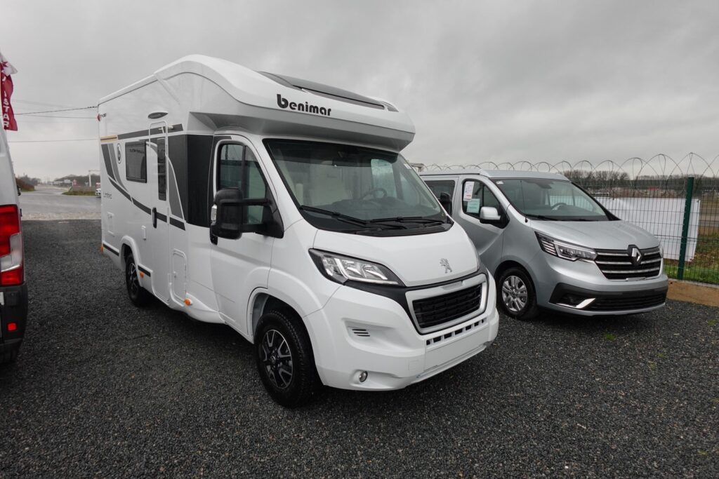 Camping-car blanc stationné à côté d'un van gris.