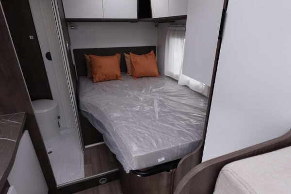 Doppelbett mit orangefarbenen Kissen im Wohnwagen