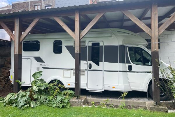 Wohnmobil weiß unter einem Holzunterstand geparkt.