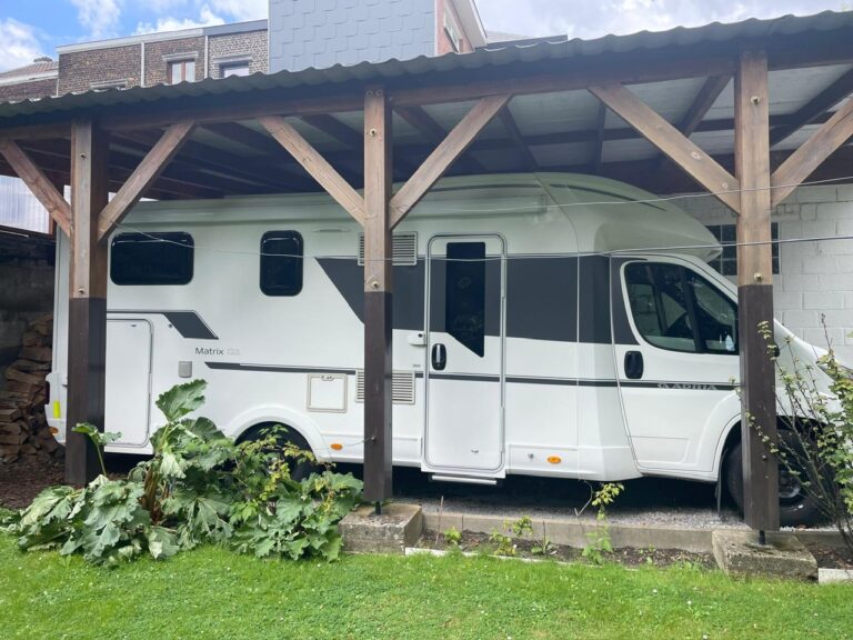 Camping-car blanc garé sous un abri en bois.
