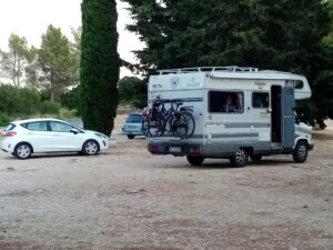 Camping-car avec vélos sur un parking boisé.