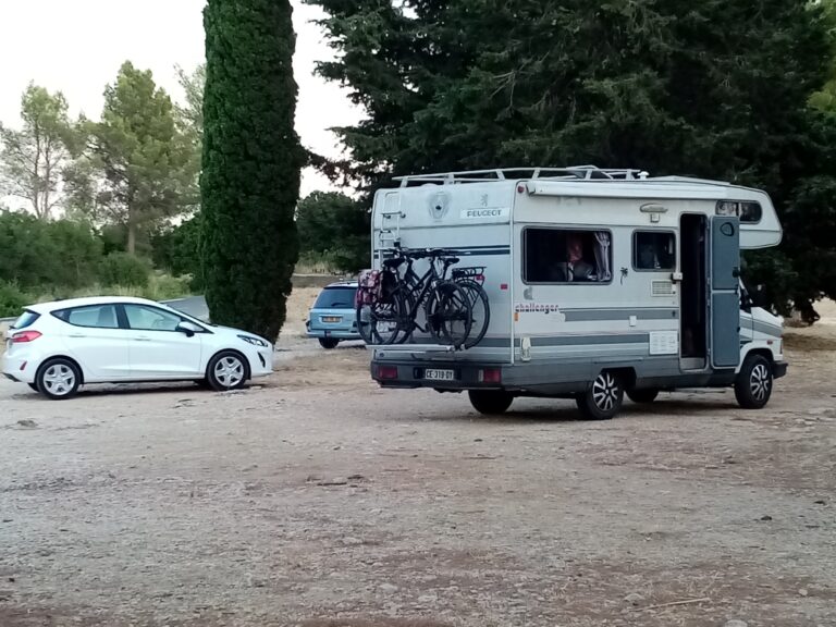 Camping-car avec vélos sur un parking boisé.
